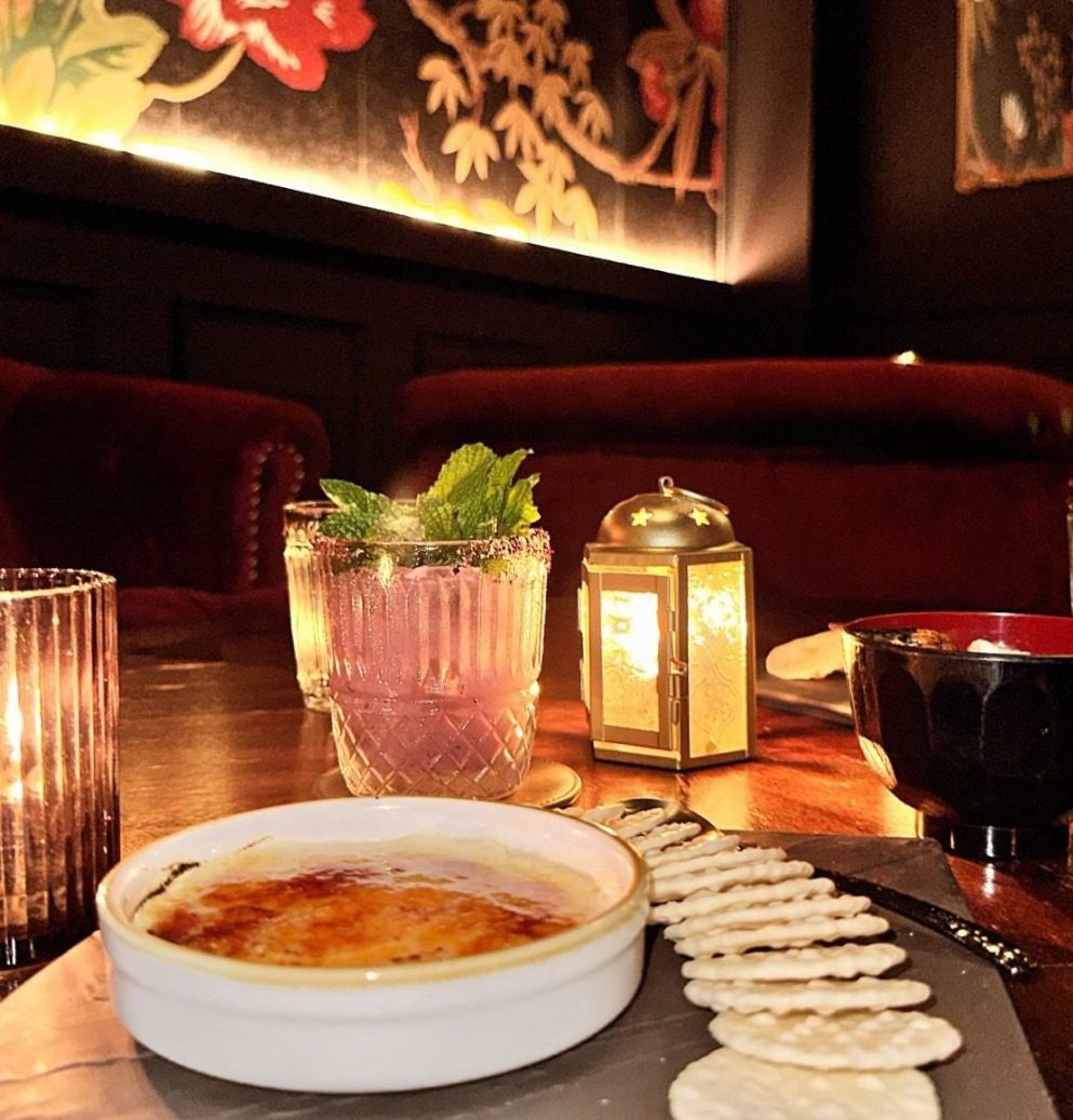 Pink cocktail garnished with mint alongside crème brûlée and rice crackers