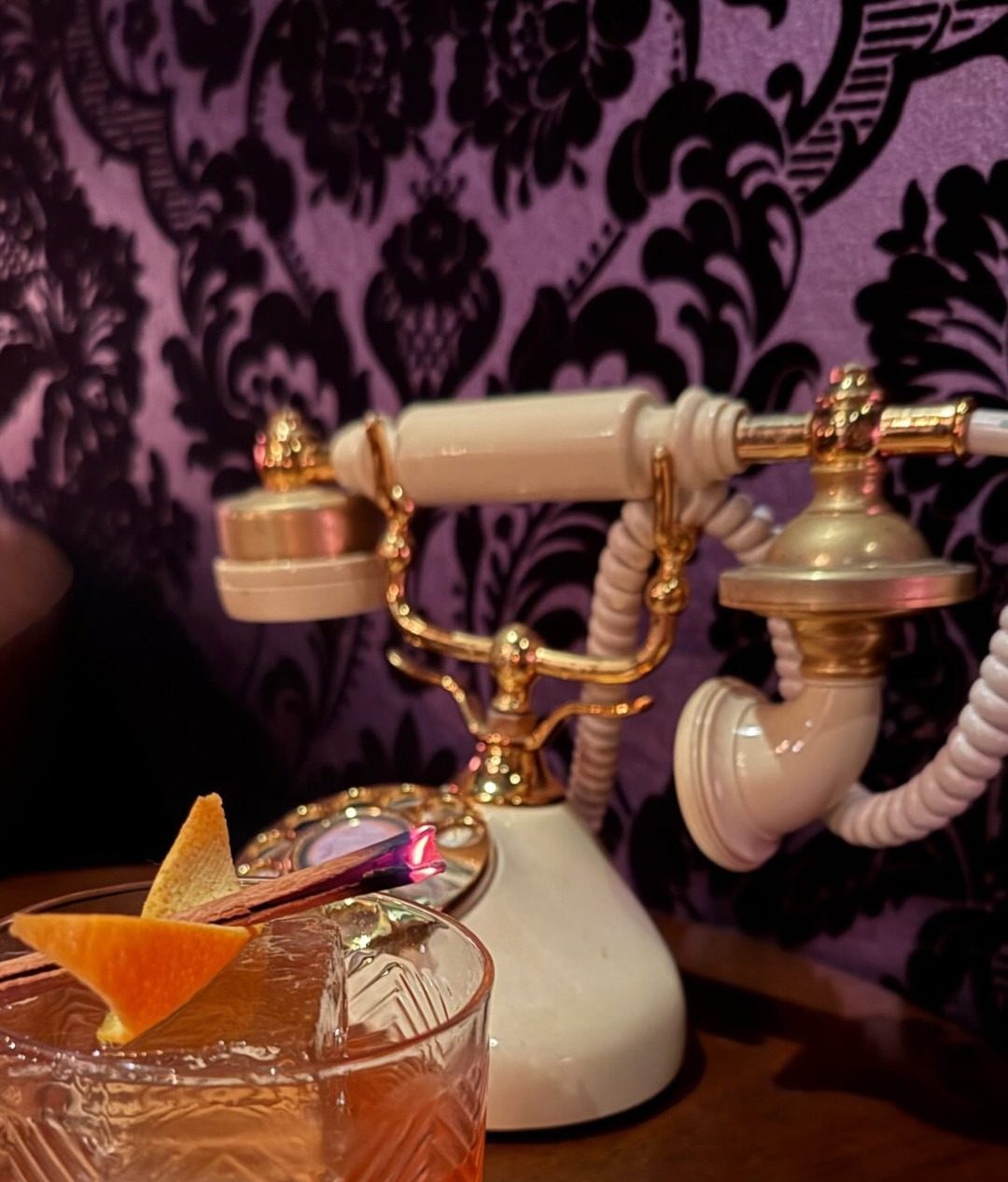 Whiskey cocktail with orange peel and cinnamon beside a vintage rotary phone